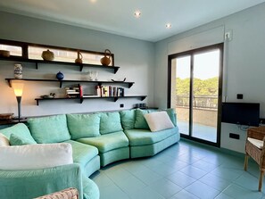 A living room with a green sofa, a flat-screen TV, and a balcony with a view. - Beautiful apartment in front of the sea (Estartit)