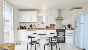 Una cucina moderna con mobili bianchi, un'isola centrale con sedute e un frigorifero integrato di grandi dimensioni.