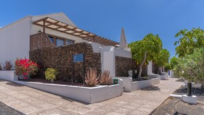 Een modern huis met een stenen muur, een pergola en diverse plantenpotten.