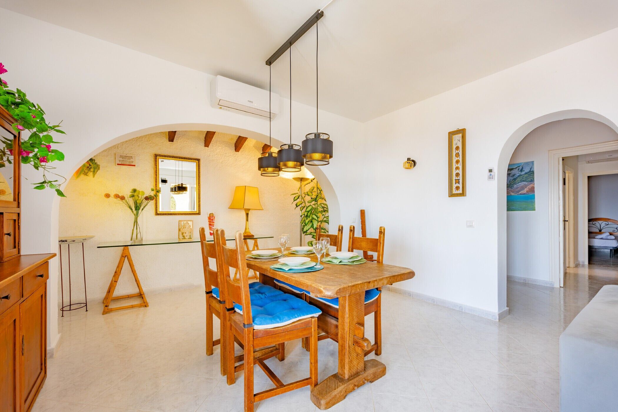 A dining area with a wooden table and chairs, a hanging light fixture, and a small side table with a lamp.