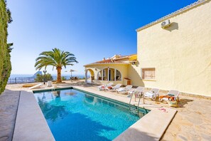 A pool area with lounge chairs, a palm tree, and a building with a tiled roof.