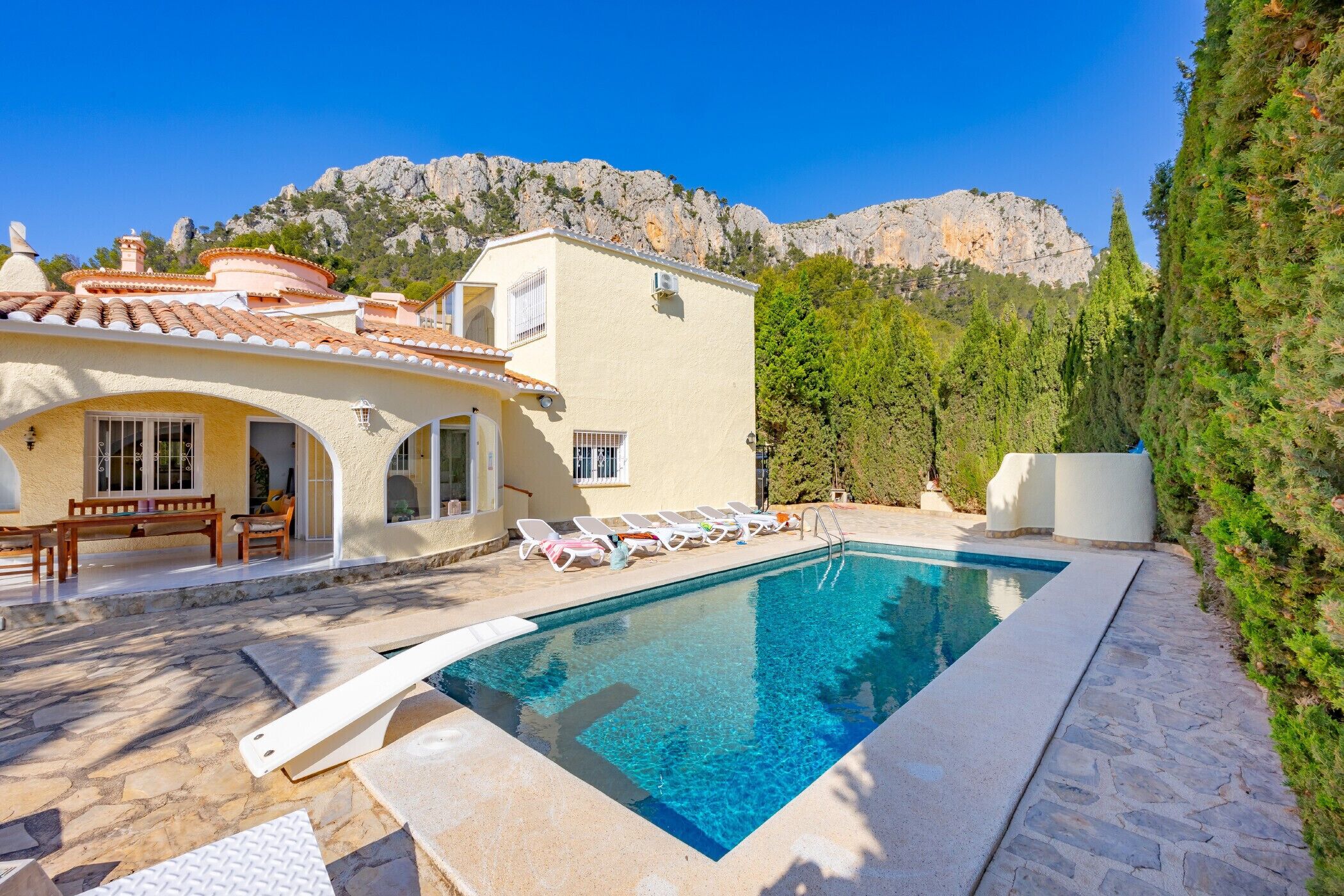 A pool area with a clear blue pool, lounge chairs, and a mountain backdrop.
