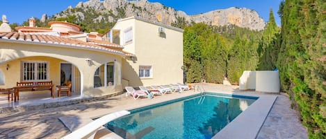 Un área de piscina con una piscina azul cristalina, sillones de descanso y un telón de fondo montañoso.