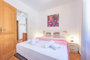 Ein Hotelzimmer mit Holztür, einem Bett mit weißen und rosa Bettwäsche, einem farbenfrohen abstrakten Gemälde an der Wand und einem Nachttisch mit Lampe.