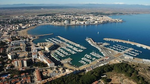 Vista aérea de una ciudad costera con un puerto deportivo, edificios residenciales y montañas al fondo.