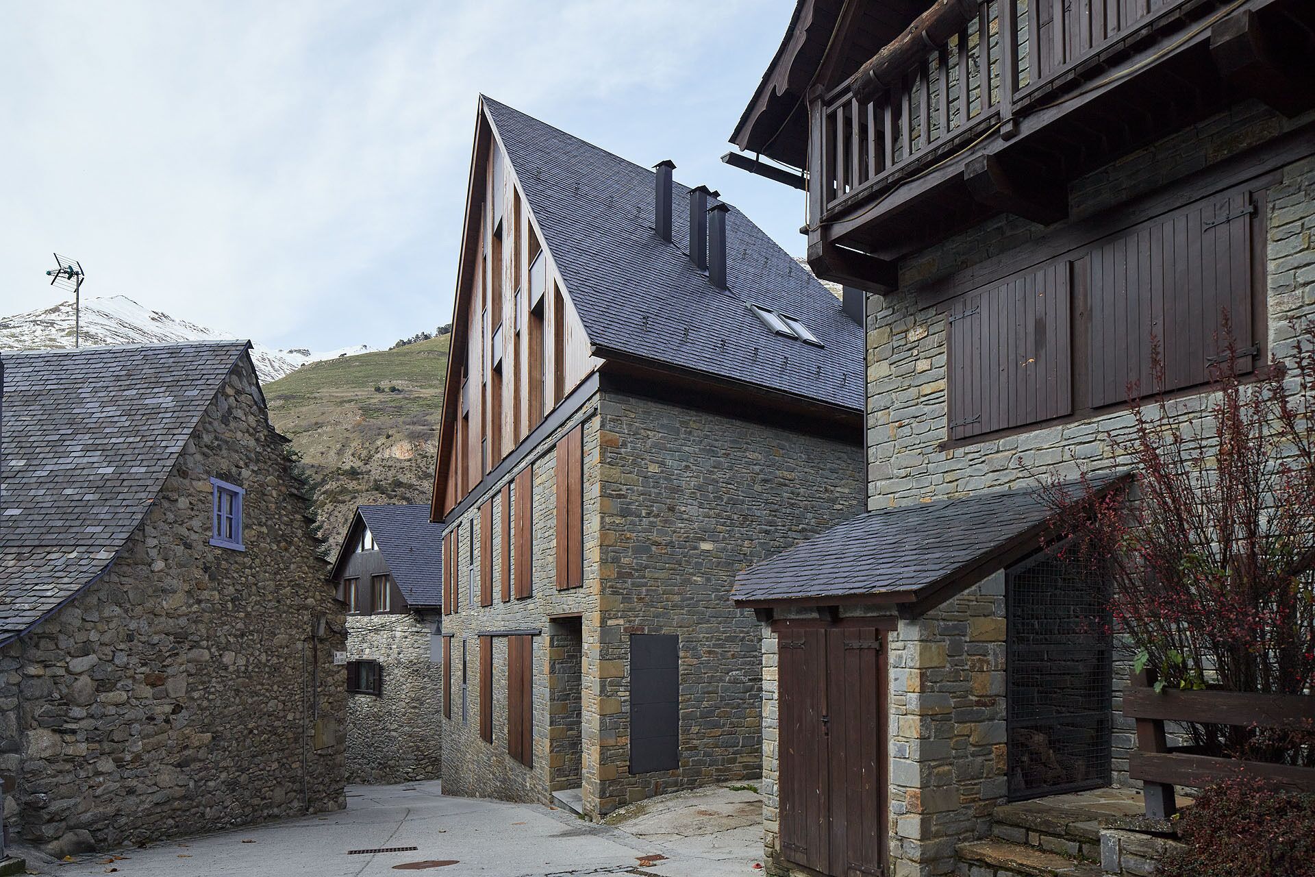 A narrow street with stone buildings, wooden balconies, and a stone wall.
