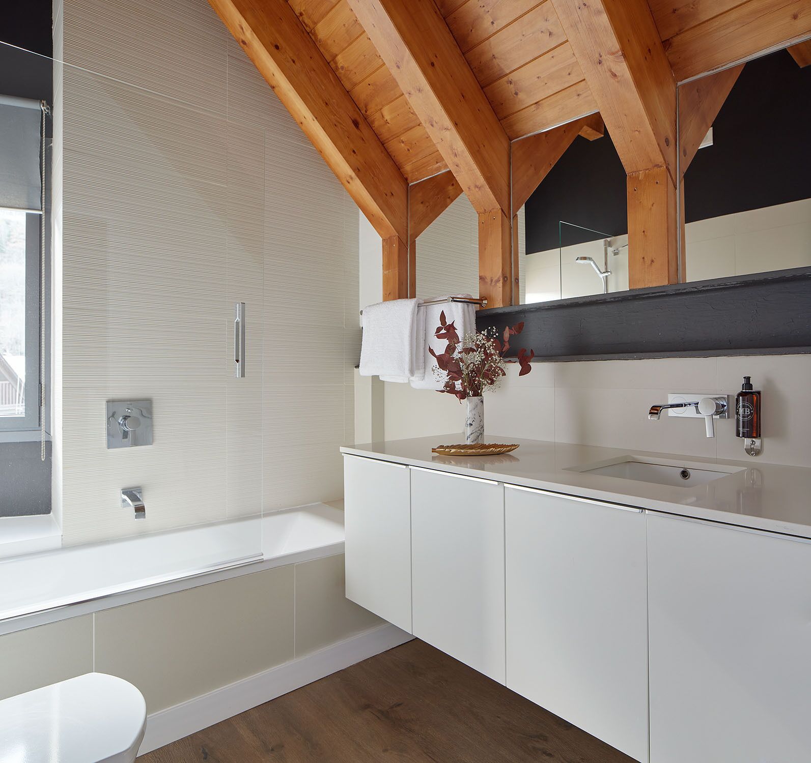 Un bagno moderno con un vanità bianca, uno specchio grande e travi di legno al soffitto.