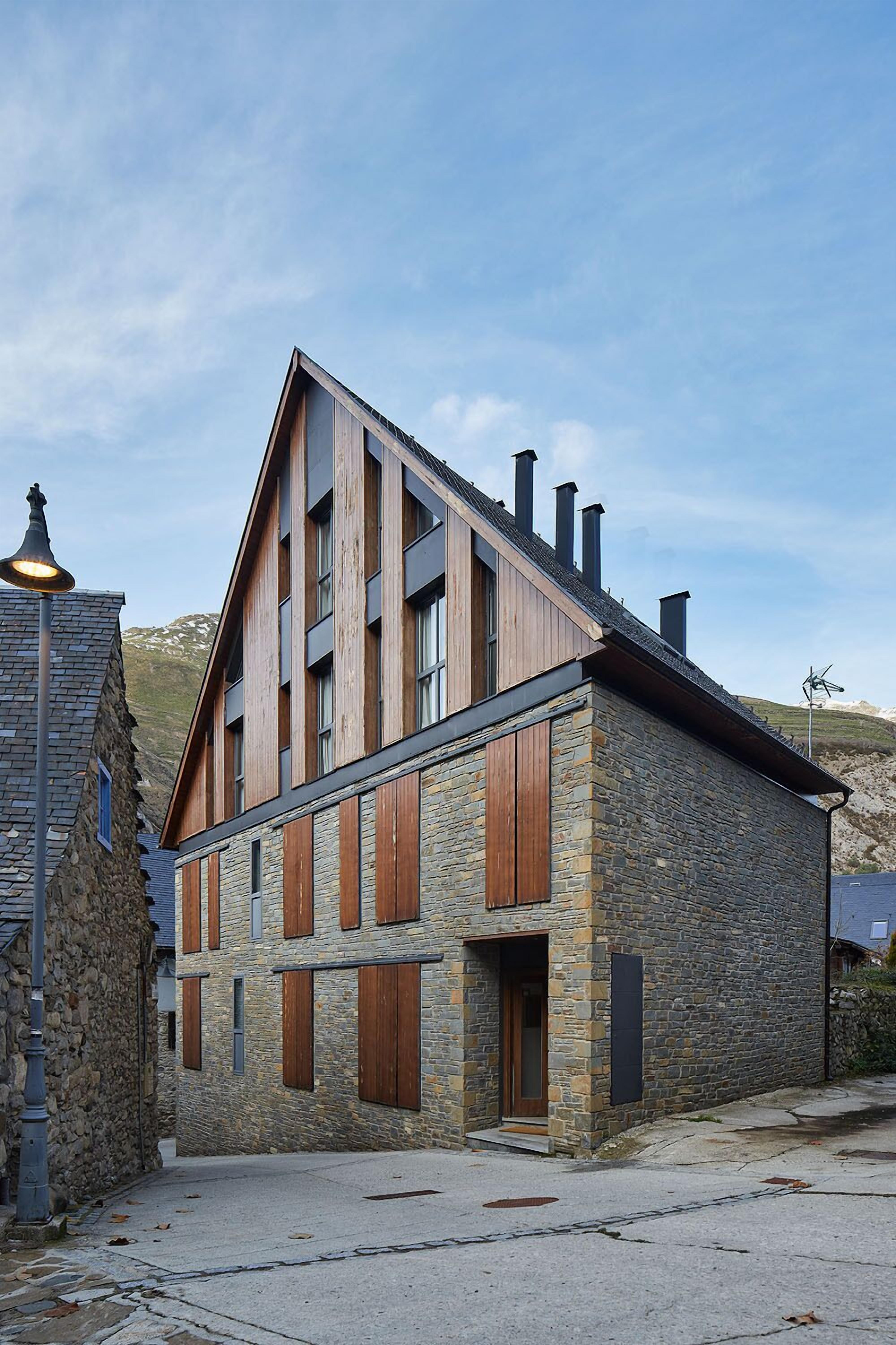 A two-story building with a stone facade and wooden shutters, featuring a steeply pitched roof and multiple chimneys.