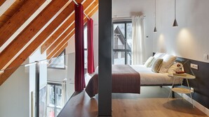 A bedroom with a sloped ceiling, a bed with pillows, a bedside table, and a window with curtains. - Val Arties 2 by FeelFree Rentals (Arties)