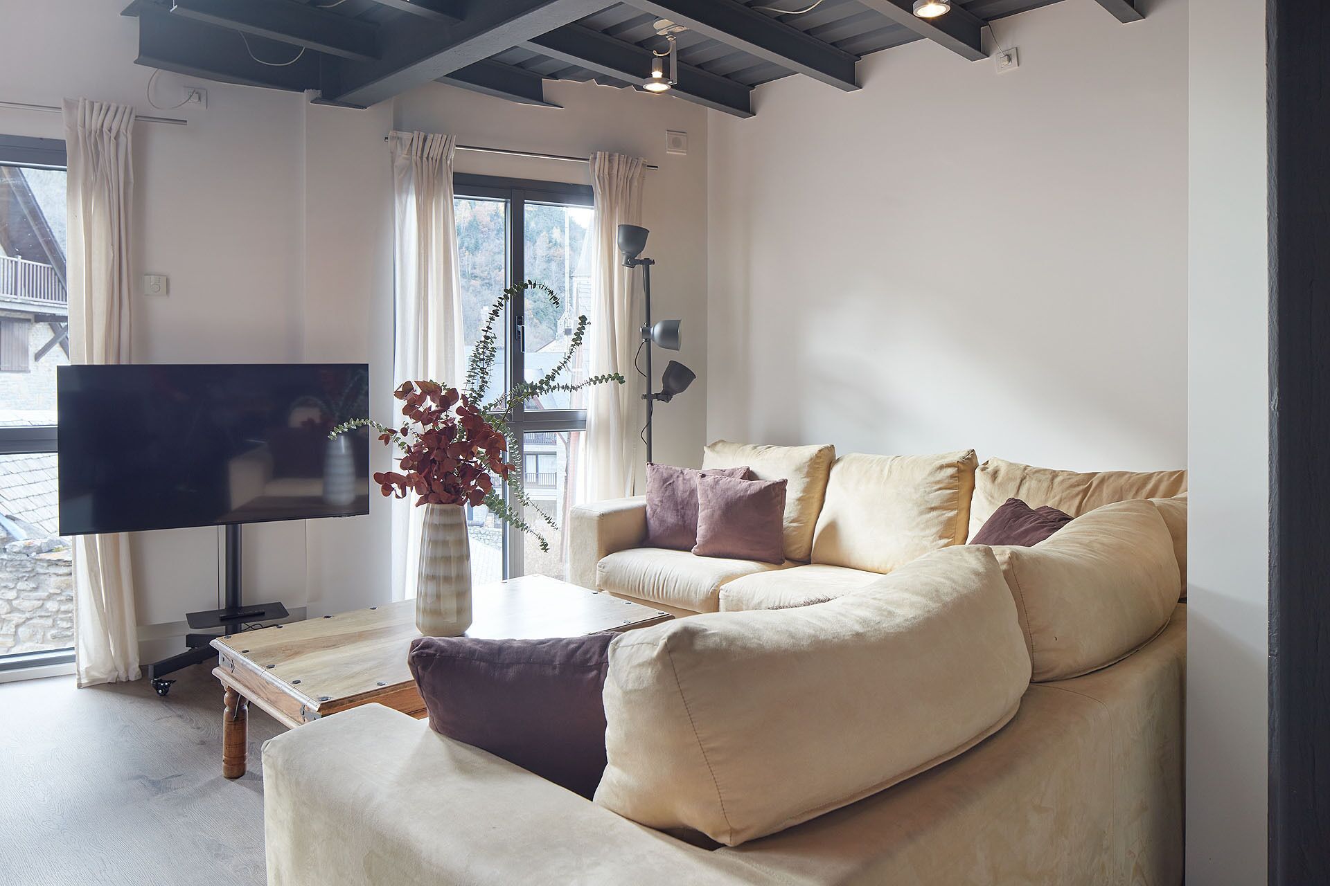 A modern living room with a sofa, a flat-screen TV, a wooden coffee table, and a vase with plants.