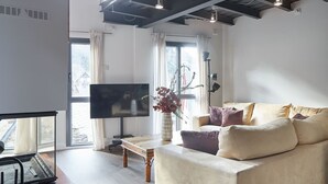 A modern living room with a flat-screen TV, a sofa with cushions, a wooden coffee table, and a vase with plants. - Val Arties 2 by FeelFree Rentals (Arties)