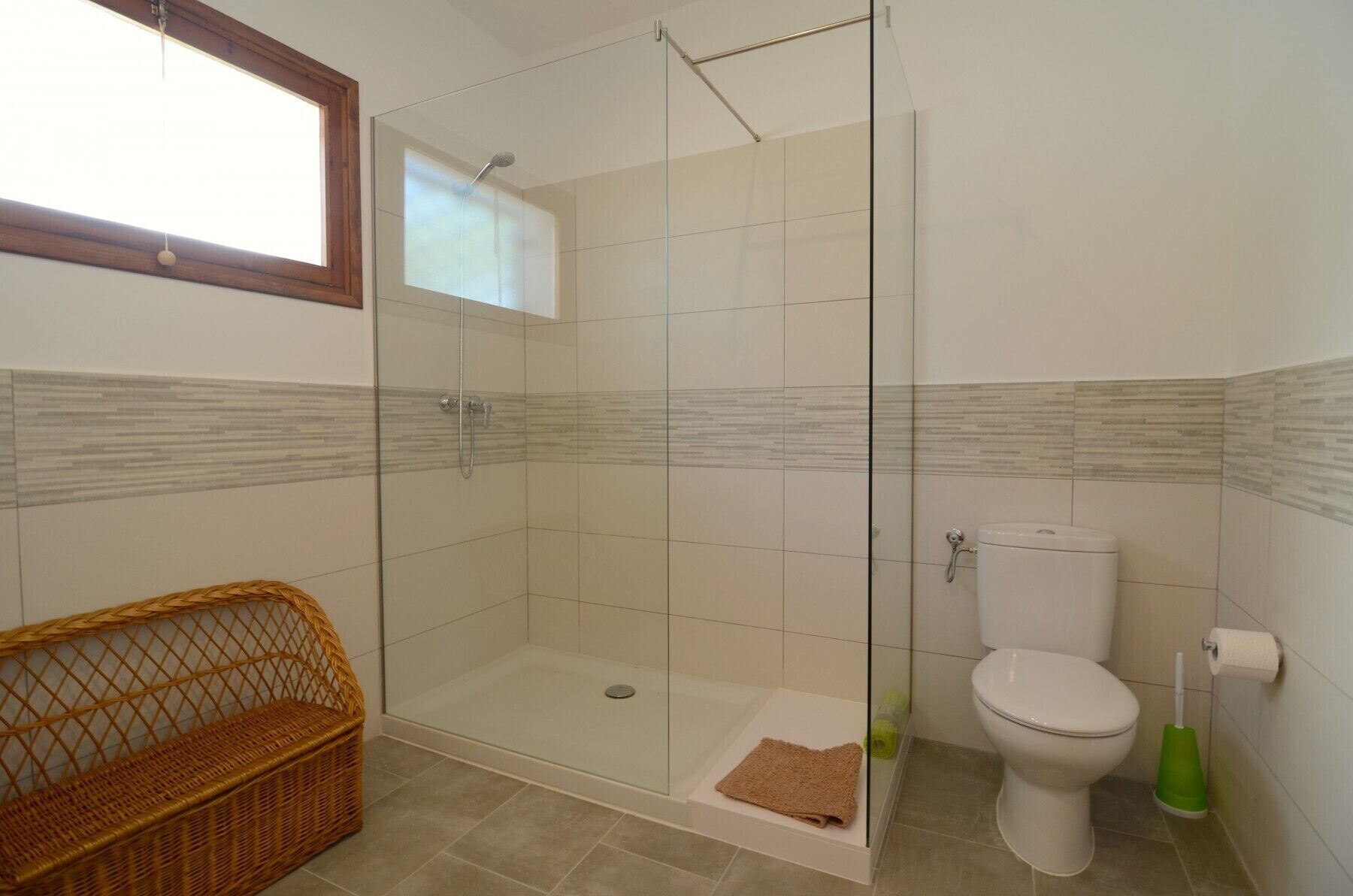 A bathroom with a glass shower enclosure, a toilet, and a wicker basket.