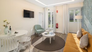 Une chambre d’hôtel moderne dotée d’une télévision à écran plat, d’un coin repas avec une table et des chaises, d’un canapé et d’une grande fenêtre avec des rideaux.