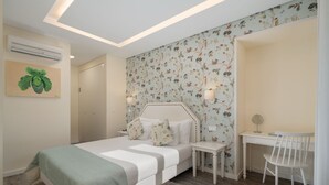 Une chambre à coucher comprenant un lit, une table de chevet, une chaise et un bureau avec une autre chaise. Un climatiseur est fixé au mur, et un tableau est accroché au mur.