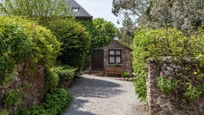 A gravel path leading to a stone building with a wooden bench and a small garden area. - Allerford Cottage, Near Dunster (Near Dunster)