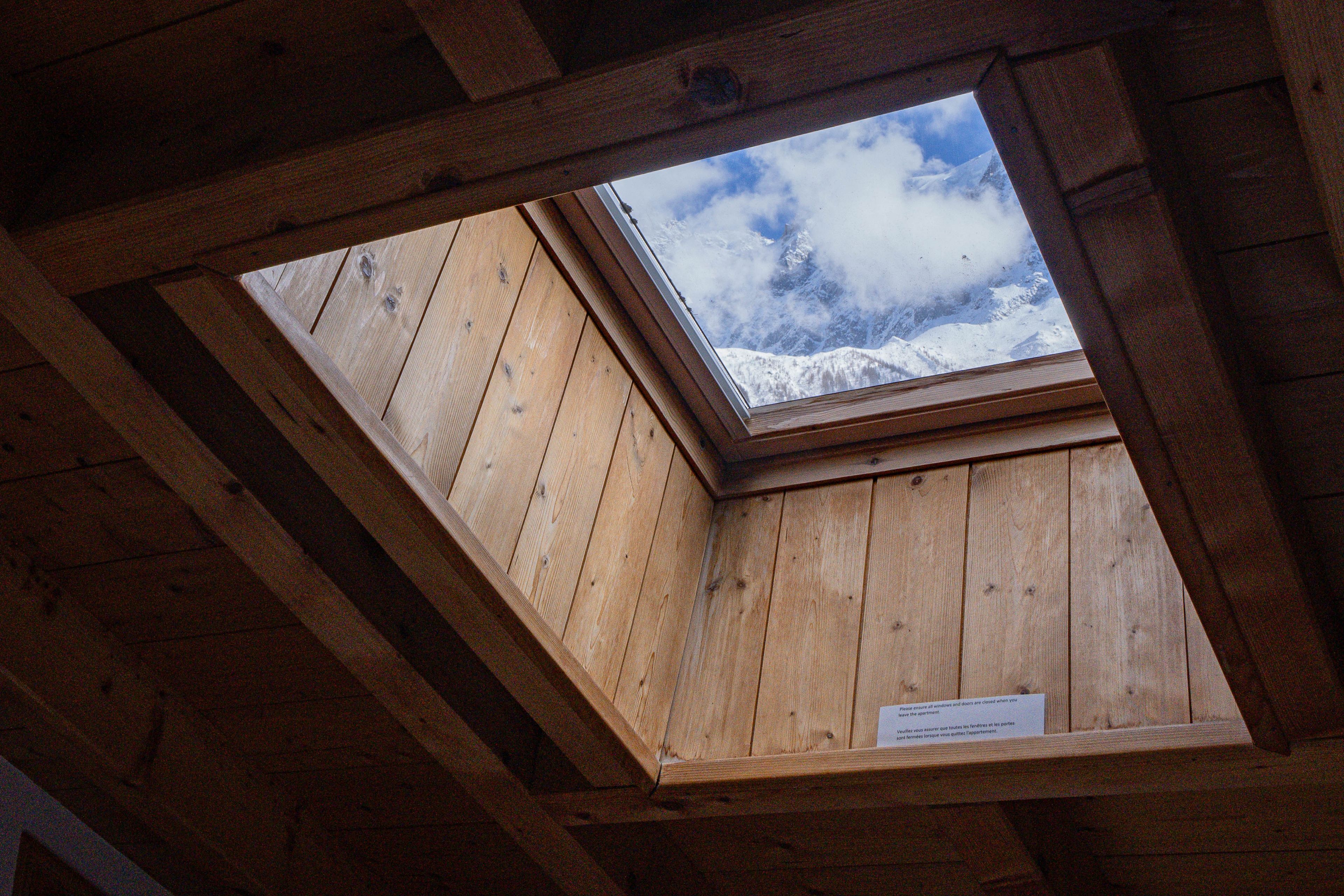 A skylight in a wooden room with a view of snow-capped mountains.