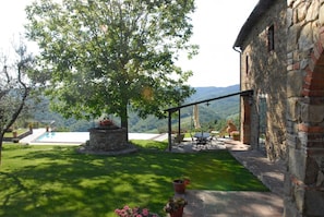 A stone building with a pool, outdoor seating, and a view of the mountains.