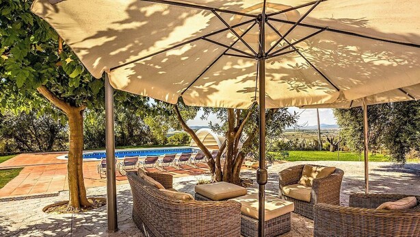 An outdoor seating area with wicker furniture and a large umbrella providing shade. - Country Chateau for 22 persons - close to Sitges! (Castellet i la Gornal)