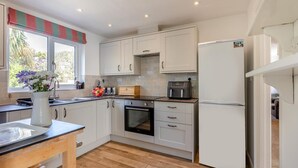Una cocina moderna con armarios blancos, encimera de madera, horno empotrado, refrigerador y ventana con cortina a rayas.