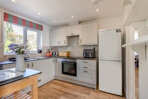 Une cuisine moderne avec des armoires blanches, un plan de travail en bois, un four encastré, un réfrigérateur et une fenêtre agrémentée d’une lambrequin à rayures.