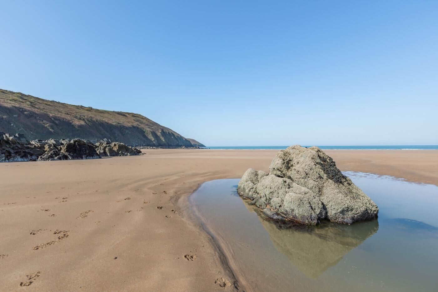 A sandy beach with a large rock in the center and a clear sky.