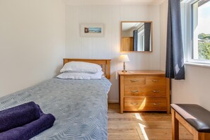 A bedroom with a bed, a bedside table with a lamp, a dresser, a bench, and a window with curtains. - 3 Bed in Braunton (oc-salar) (Georgeham)