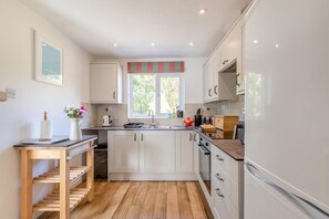 A modern kitchen with white cabinets, a wooden countertop, and a window with a striped valance. - 3 Bed in Braunton (oc-salar) (Georgeham)