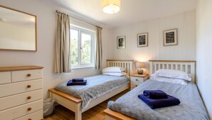 Un dormitorio con dos camas individuales, un aparador, una ventana con cortinas y cuadros colgados en la pared.