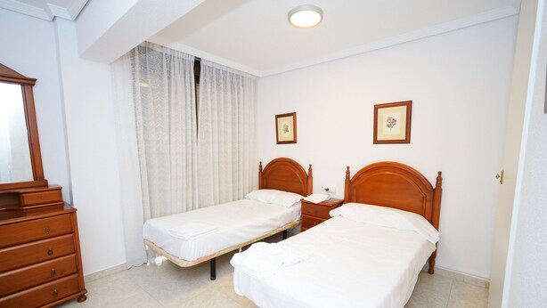 Un dormitorio con dos camas individuales, un aparador de madera y una lámpara en el techo.