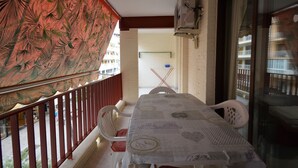 Un balcón con mesa y sillas, barandilla roja y vista a la calle y los edificios.