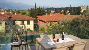 A terrace with a table set for two, overlooking a residential area with red-tiled roofs and greenery.