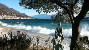 A coastal scene with a statue, a pebble beach, and a town in the background.