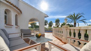 Eine Terrassengruppe im Freien mit weißer Wand, Glastisch und beigefarbenen Sitzkissen.