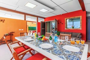 Ein Essbereich mit einem langen Tisch, gedeckt für vier Personen, umgeben von Holzstühlen mit roten Kissen.