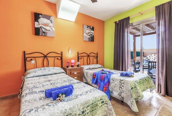 Habitación de hotel con dos camas, un balcón con mesa y sillas, y obras de arte en las paredes.