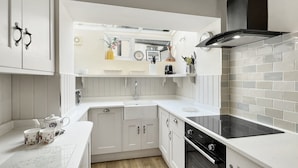 A modern kitchen with white cabinetry, a black stove, and a backsplash of white tiles. - Grace Cottage, Porlock (Porlock)