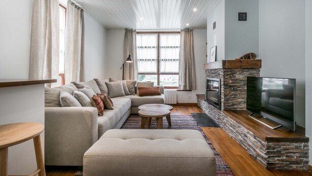 A modern living room with a sectional sofa, a flat-screen TV, a stone fireplace, and a large window with curtains. - Era Solana by FeelFree Rentals (Vielha)