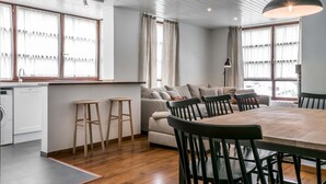 A modern kitchen with a built-in dishwasher, wooden stools, a dining table with chairs, and a sofa in a bright living area with large windows. - Era Solana by FeelFree Rentals (Vielha)
