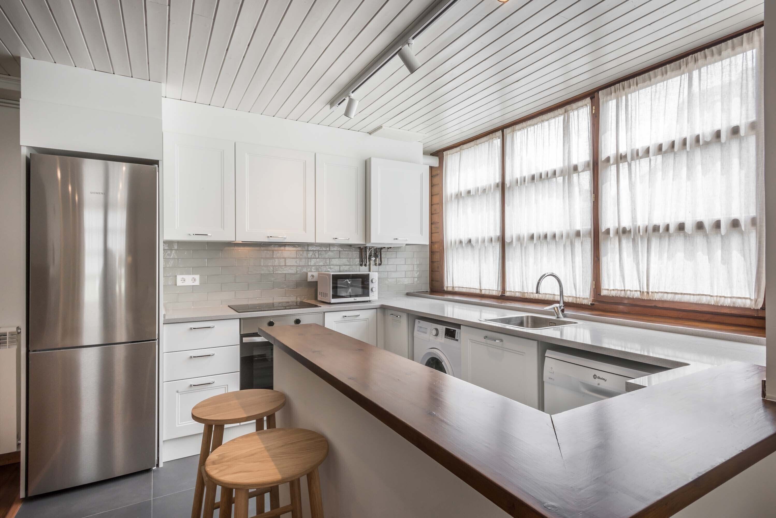 A modern kitchen with white cabinets, stainless steel appliances, and a wooden island with stools.