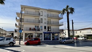 A multi-story building with balconies, a storefront, and parked cars. - APARTAMENT GRECIA (Estartit)