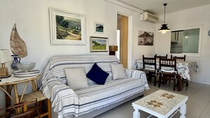 A cozy living room with a striped sofa, a dining table with chairs, and various framed pictures on the walls. - APARTAMENT GRECIA (Estartit)