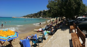 A beach with people sunbathing, a sandy shore, and a clear blue sea.