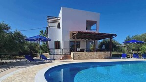 A modern pool area with stone flooring, a white building, and blue umbrellas. - Villa near Almyrida ☀️ Private Pool Gated For Child Safety ☀️ FREE WiFi (Old Road, Gavalochori - Almyrida)