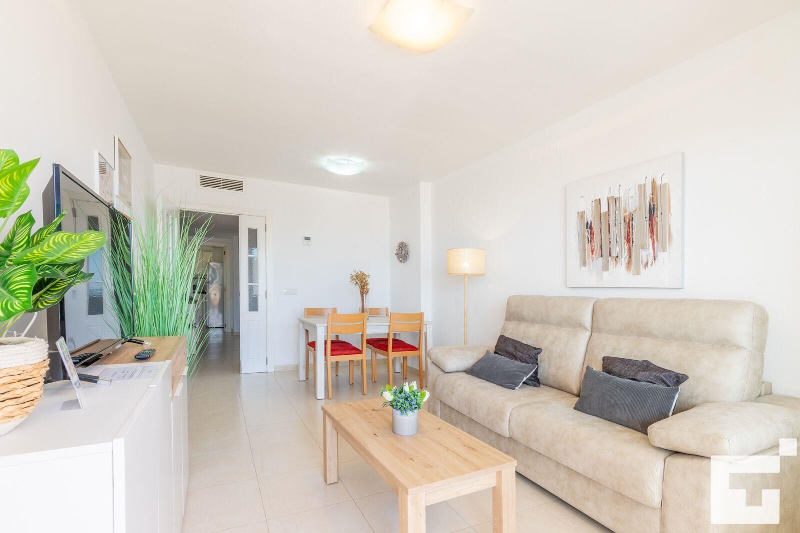 A modern living room with a beige sofa, wooden coffee table, and a dining area with a white table and chairs.
