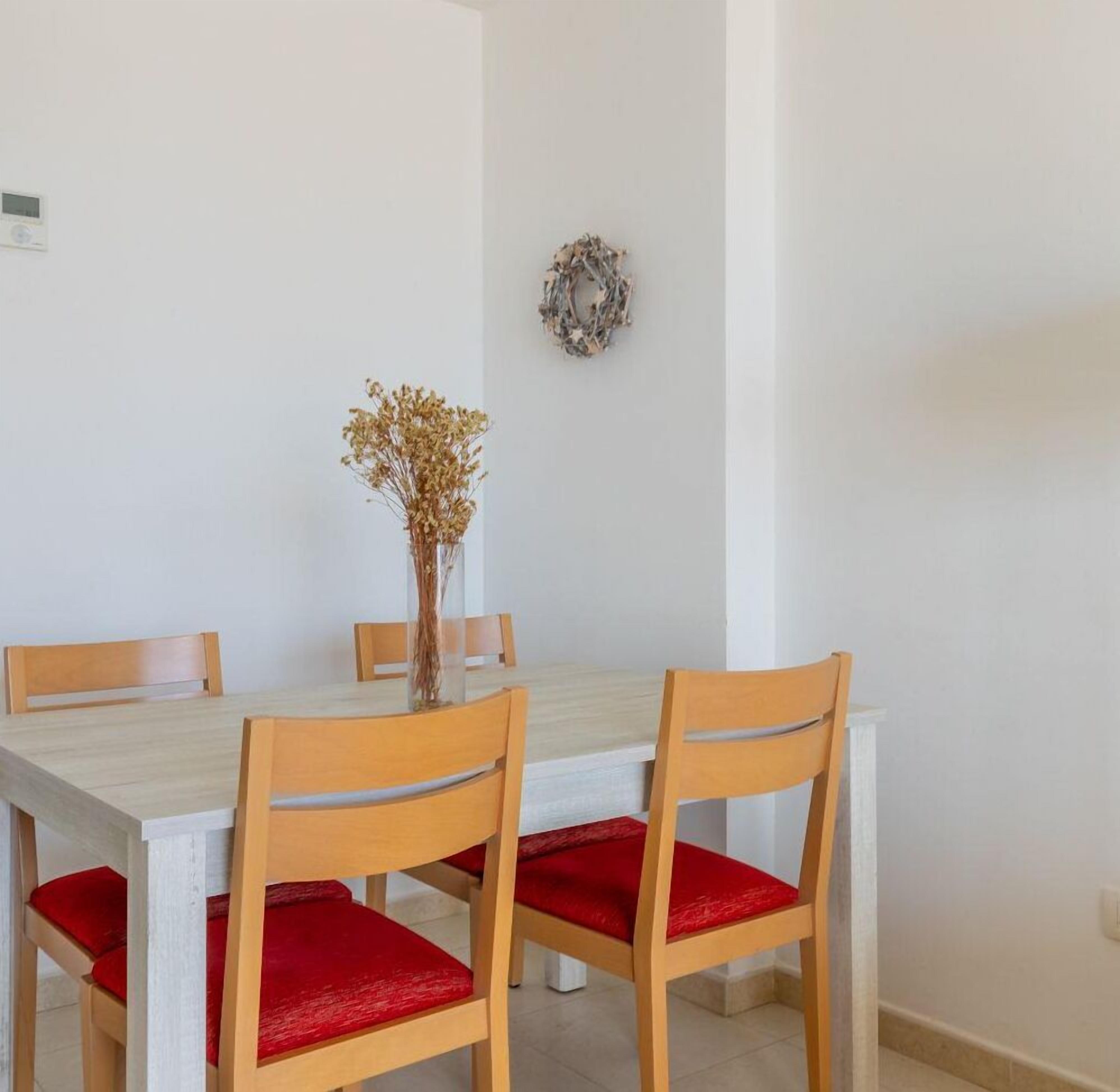 A dining area with a white table and wooden chairs with red cushions.