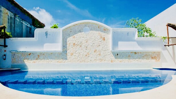 A swimming pool with a stone wall and a clear blue sky.