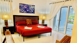 A hotel room with a large bed, two bedside lamps, a wooden bench, and a view through a sliding glass door.