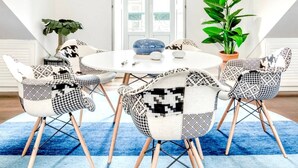 A dining area with a round table, patterned chairs, a blue rug, and a hanging light fixture.