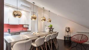 A modern kitchen with a central island, white cabinets, and a red backsplash. There are three pendant lights, a black chair, and a red chair.