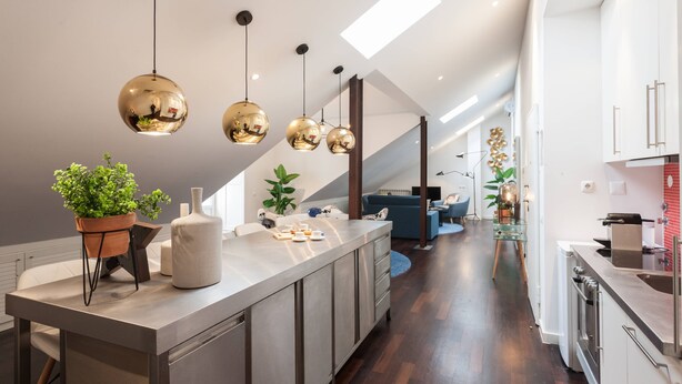 A modern kitchen with a central island, pendant lighting, and a view to the living area.